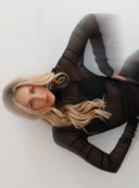 Zbliżenie na opartą o ścianę modelkę w czarnej przezroczystej bluzce Muse