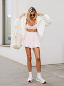 Modelka w pudroworóżowym topie Bra Run, tenisowej spódniczce oraz jasnej bluzie