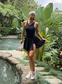 Modelka w czarnej sukience sportowej Dress Halo i jasnych butach na tle roślinności