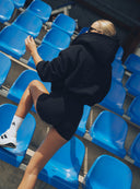 Gładki tył czarnej bluzy z kapturem Hoodie Club Black na modelce na trybunach