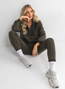 Siedząca modelka w komplecie dresowym z ciemnooliwkową bluzą Ines oraz sneakersami