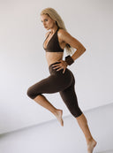 Modelka w pozie z boku w brązowych legginsach 3/4 Oldschool Choco i topie sportowym