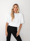 Biały T-shirt Kaia z poduszkami na ramionach w połączeniu z czarnymi spodniami