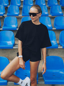 Modelka w czarnym t - shircie oversize Sunday Tee i dopasowanych kolarkach na trybunach